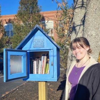 Loreley stands beside a fully stocked Little Free Library